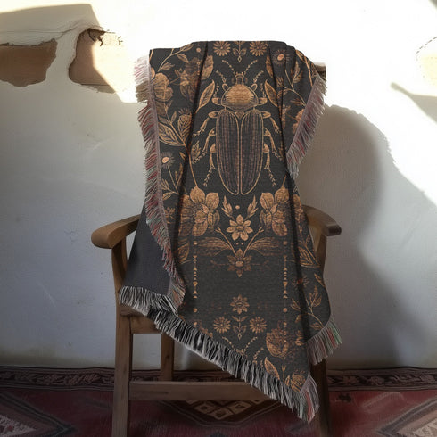 Black cotton throw blanket featuring woven bronze beetles and botanical motifs with multicolored fringe trim.